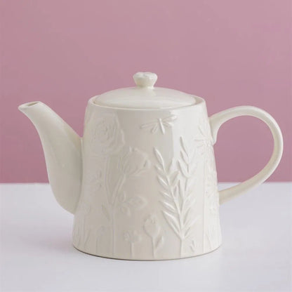 White ceramic teapot with embossed floral design on a pink background