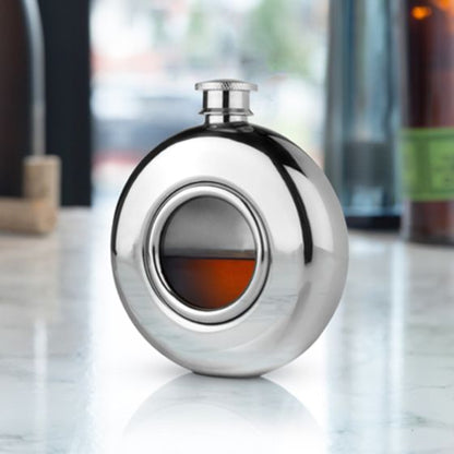 A stainless steel flask with a glass porthole window, displayed on a marble surface.