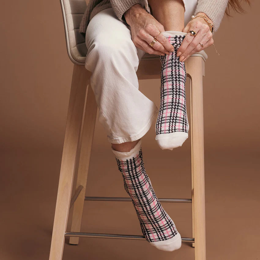 Person sitting on a stool wearing pink and black plaid socks against a brown background