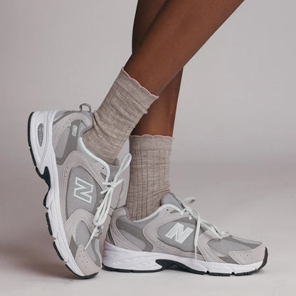 person's feet wearing Gray sneakers  and grey socks with pink trim on a neutral background