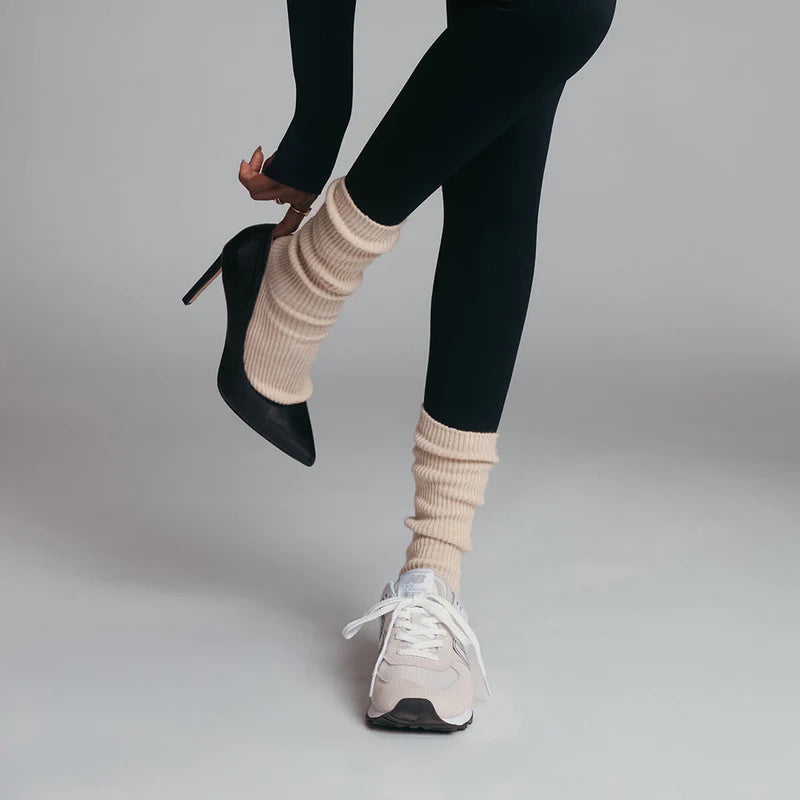 Person wearing one black high heel and one white sneaker with ivory slouch socks on a plain background