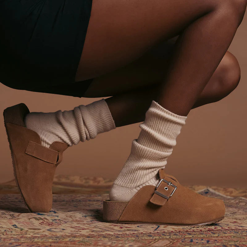 person wearing Brown clogs with buckles and ivory slouch socks on a patterned rug.