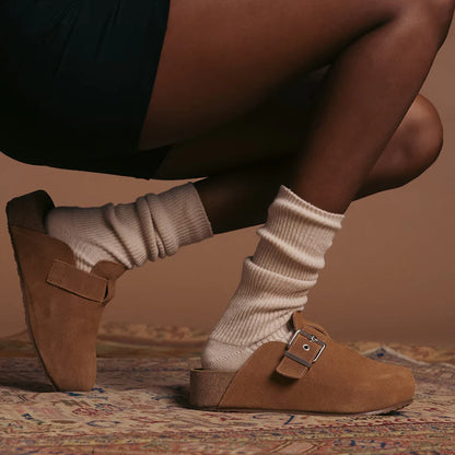 person wearing Brown clogs with buckles and ivory slouch socks on a patterned rug.