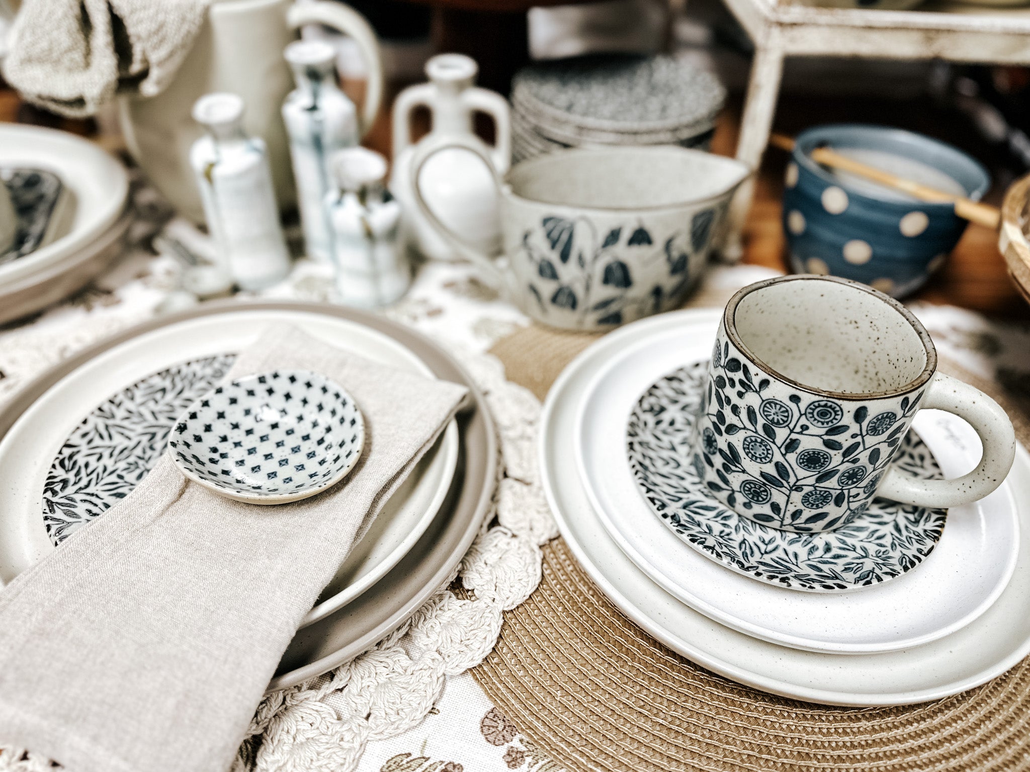 Decorative place setting including tan and brown plates and cups, crochet placemat, gravy boat and small white and blue vases.