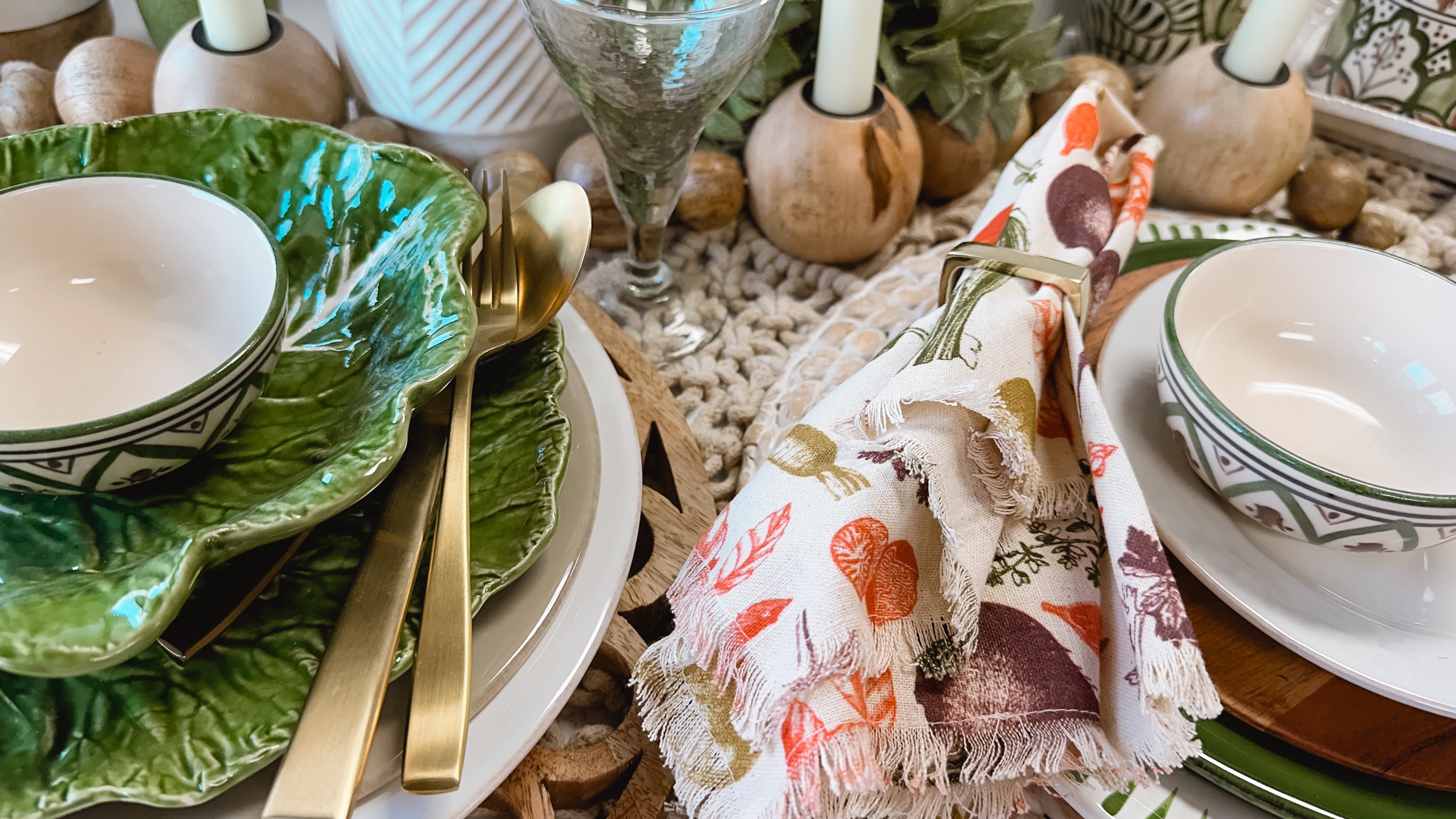 tablescape including plates, bowls, candle holders, napkins, and gold flatware