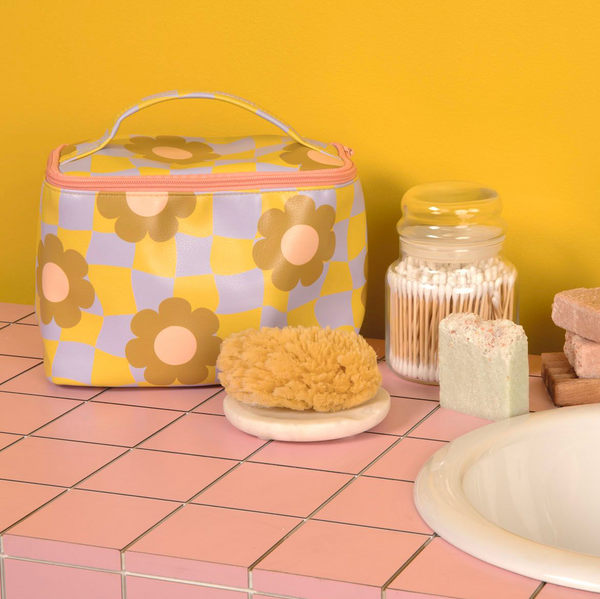 cool funky daisy cosmetic bag set on a bathroom counter with a sponge, soaps, and a jar of q-tips.