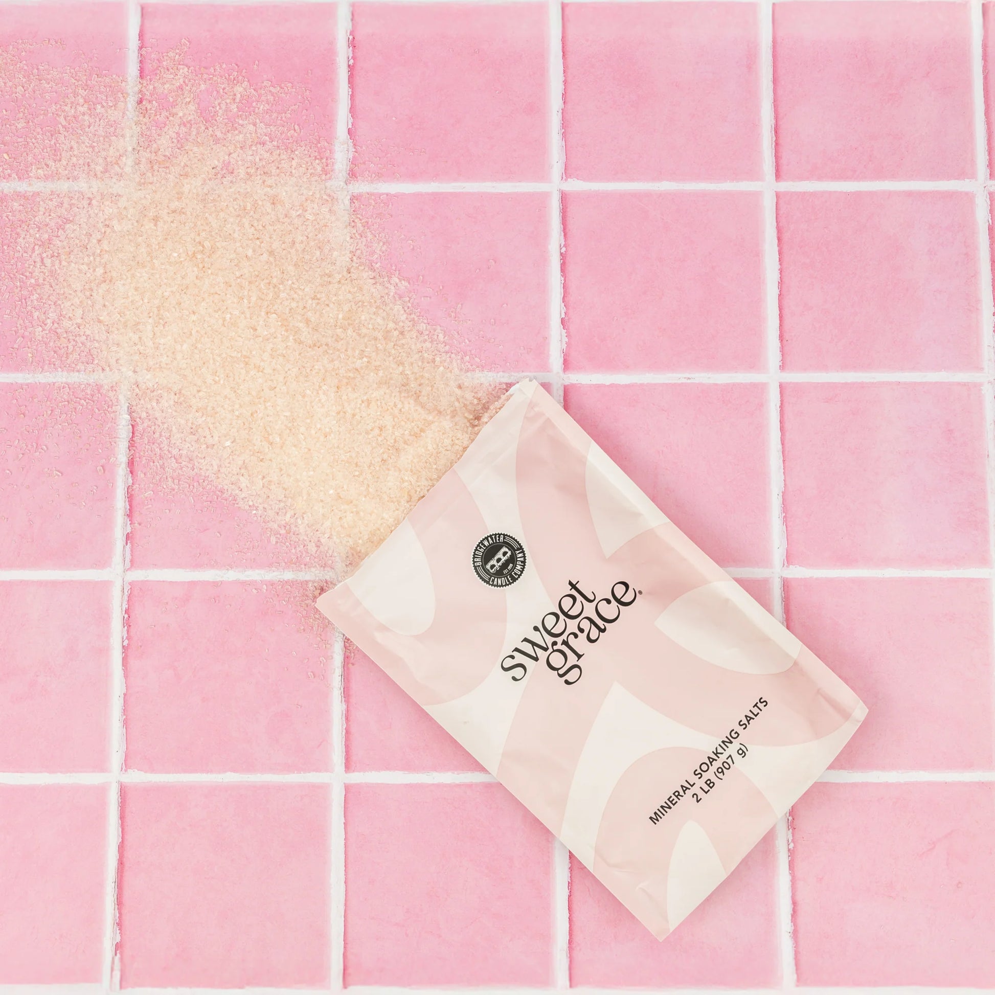 Sweet Grace mineral soaking salts coming out of the bag on a pink tiled background