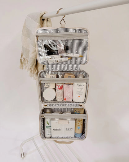 Maggie cosmetic bag open and filled with cosmetics hanging from a rod.