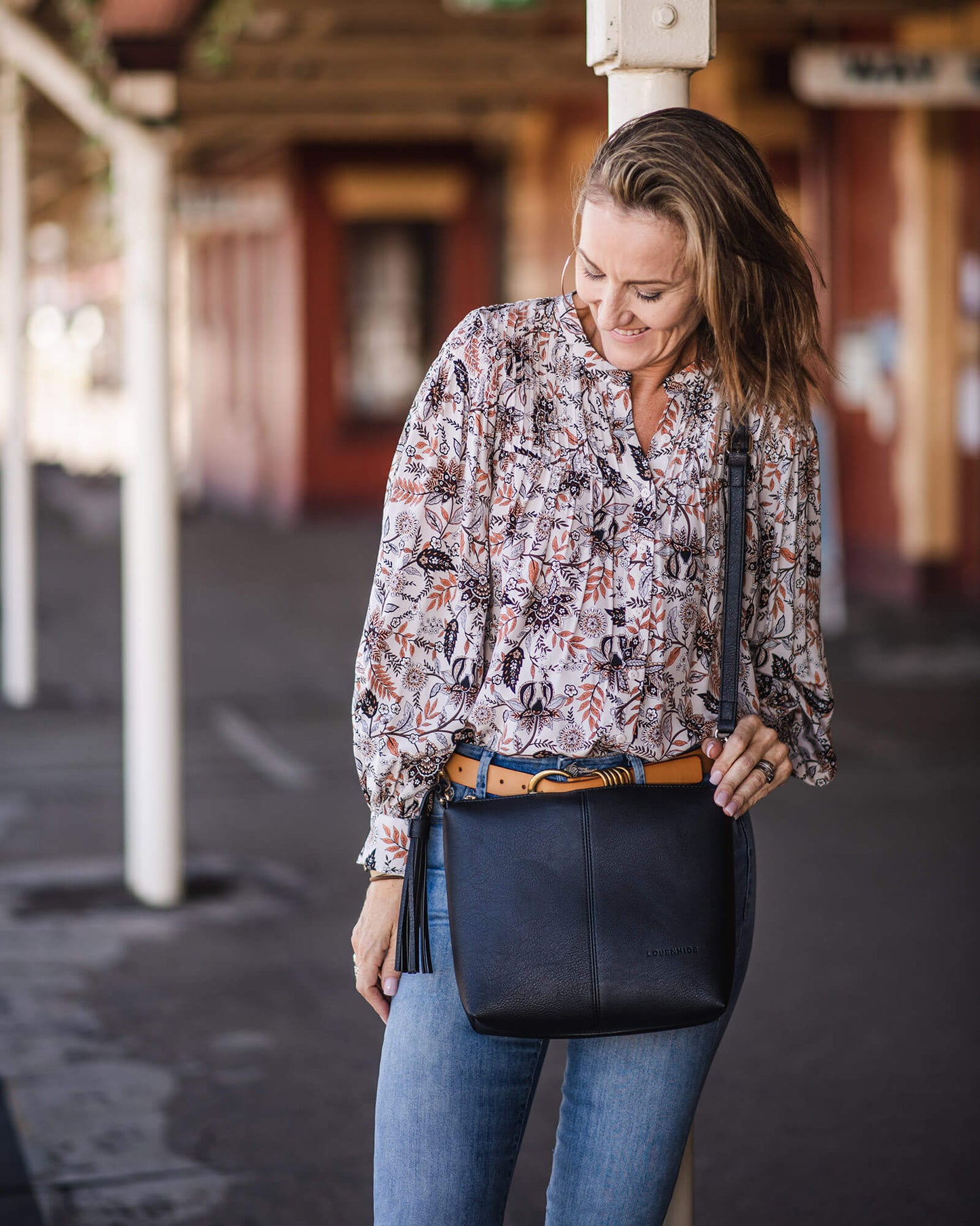 Person wearing colorful printed blouse Carrying black Daisy bag.