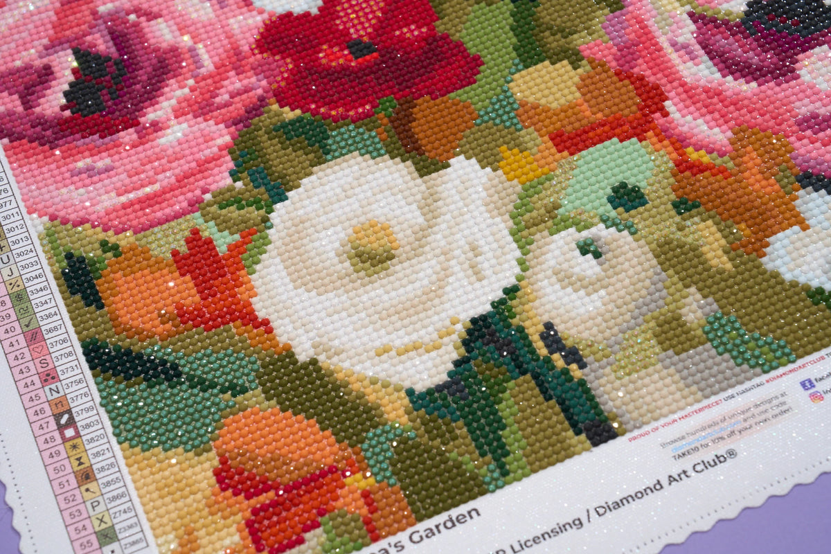 A close-up of a diamond painting of a floral design featuring white anemones, red poppies, and pink roses with green and orange foliage. A color reference chart is visible on the left side.