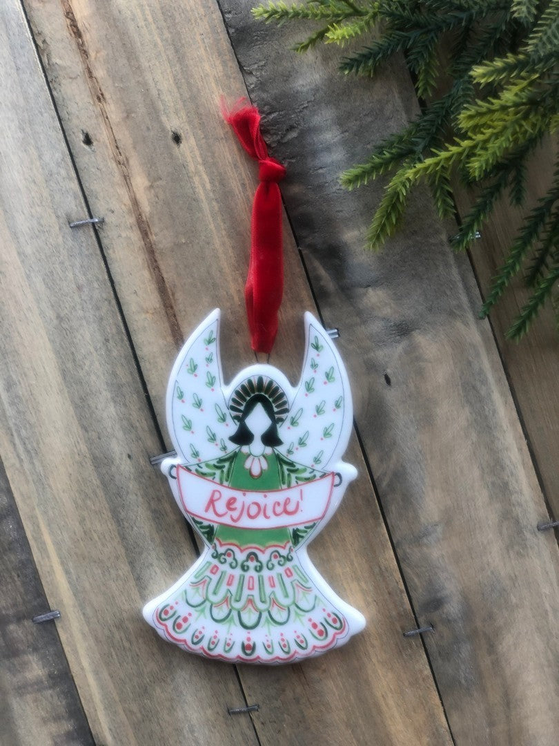 ceramic angel ornament laying on a wood slat background with greenery next to it.