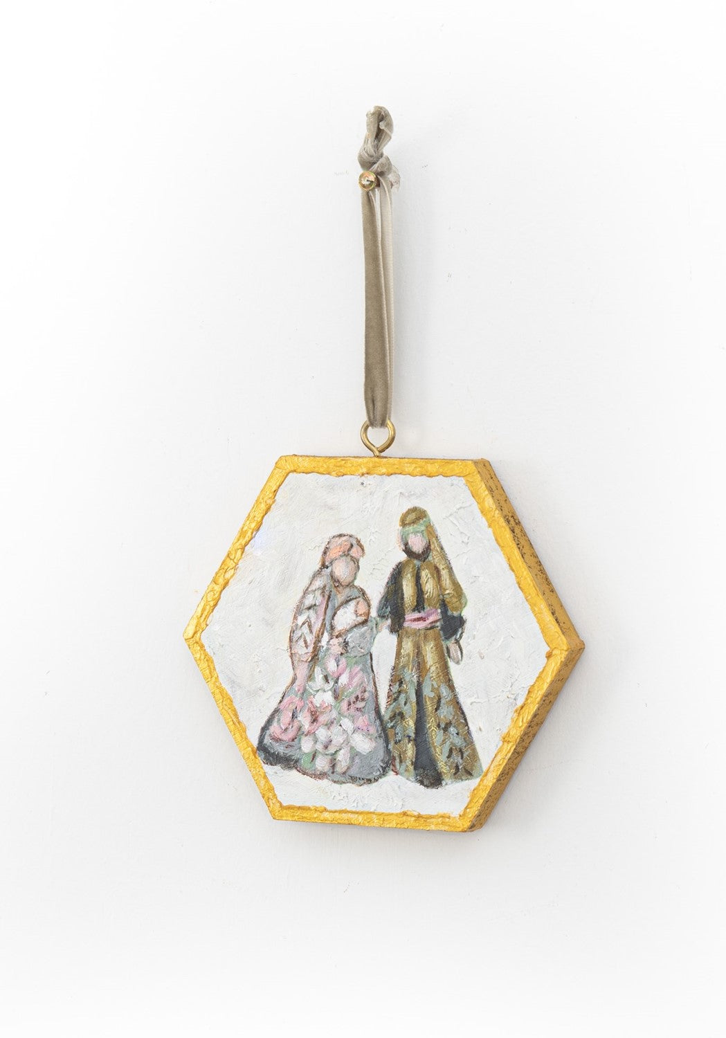 hexagon nativity ornament hanging from a taupe velvet ribbon on a white background.