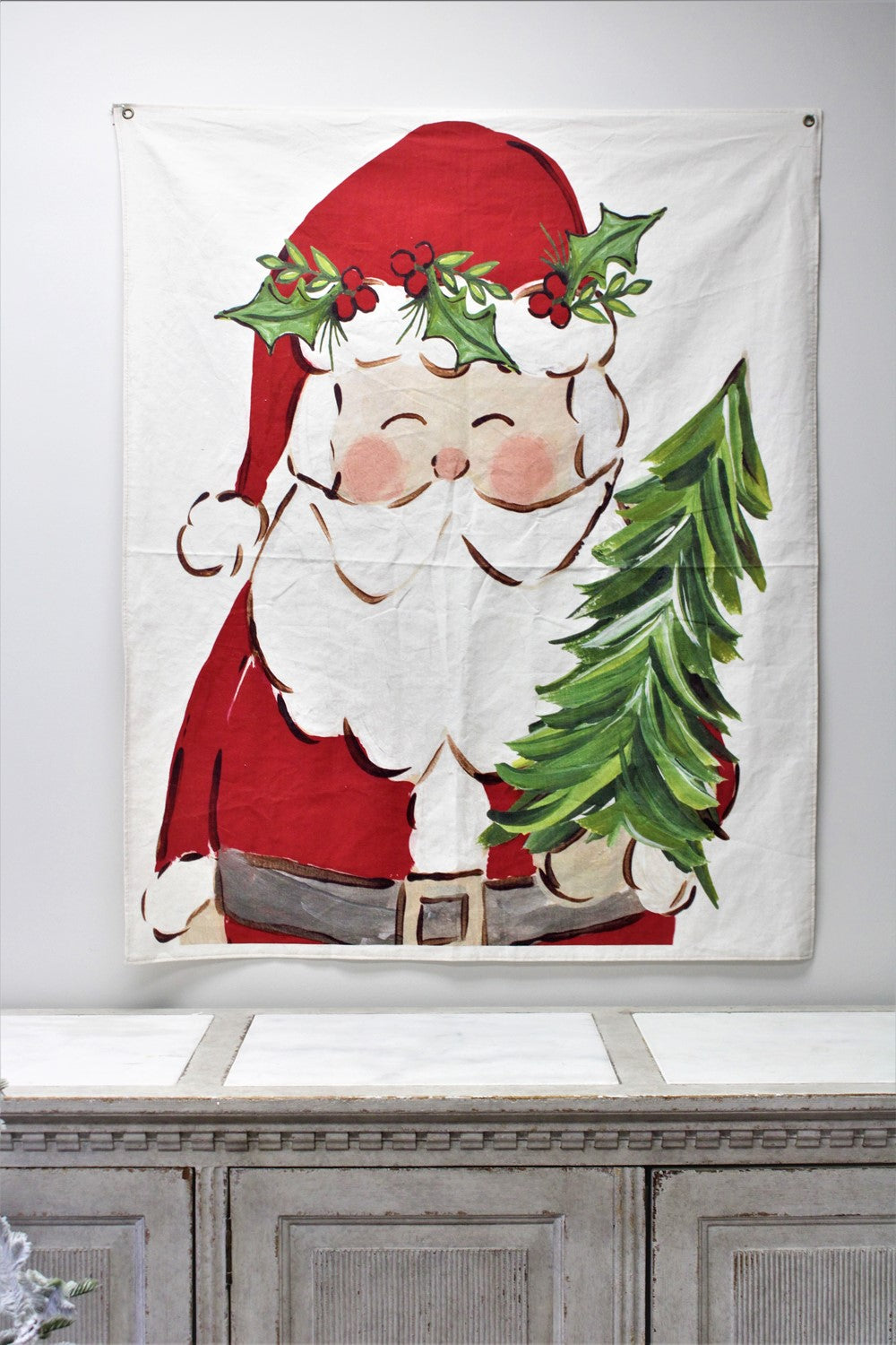 santa holding a tree fabric wall hanging displayed on a wall above a light wood console