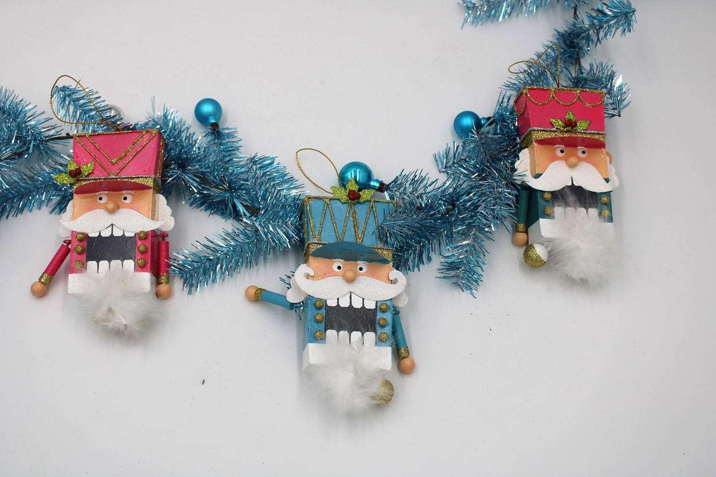 3 pink and teal metal nutcrackers arranged with a piece of tinsel.