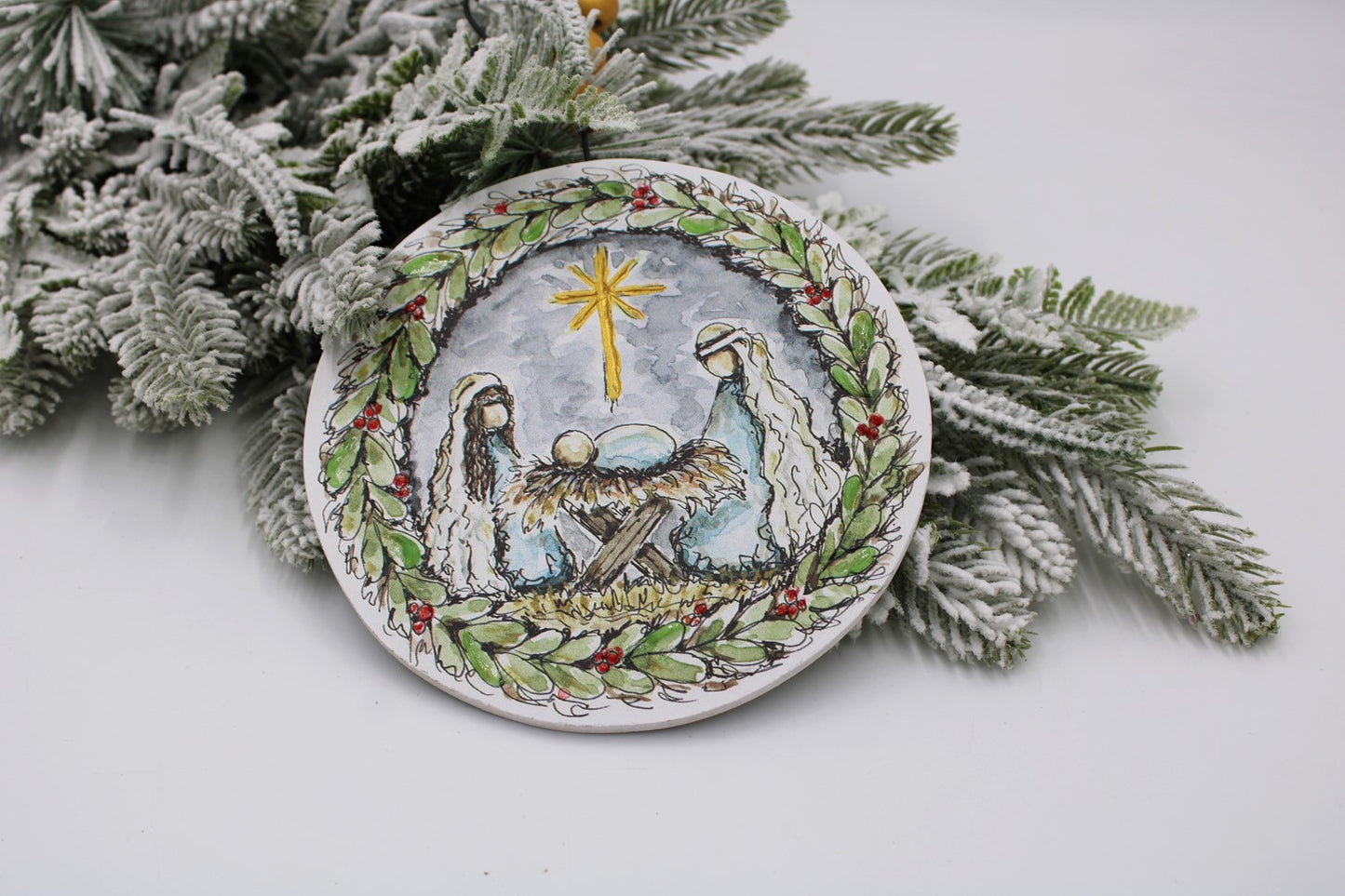 nativity ornament set on a sprig of greenry.