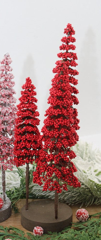 3 red berry trees on a round wooden base arranged on a table with greenery