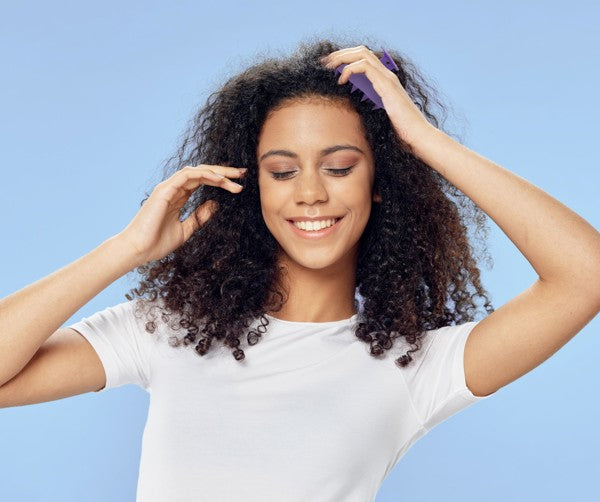 a woman using the Love Your Locks Wet & Dry Scalp Massager on her scalp against a blue background