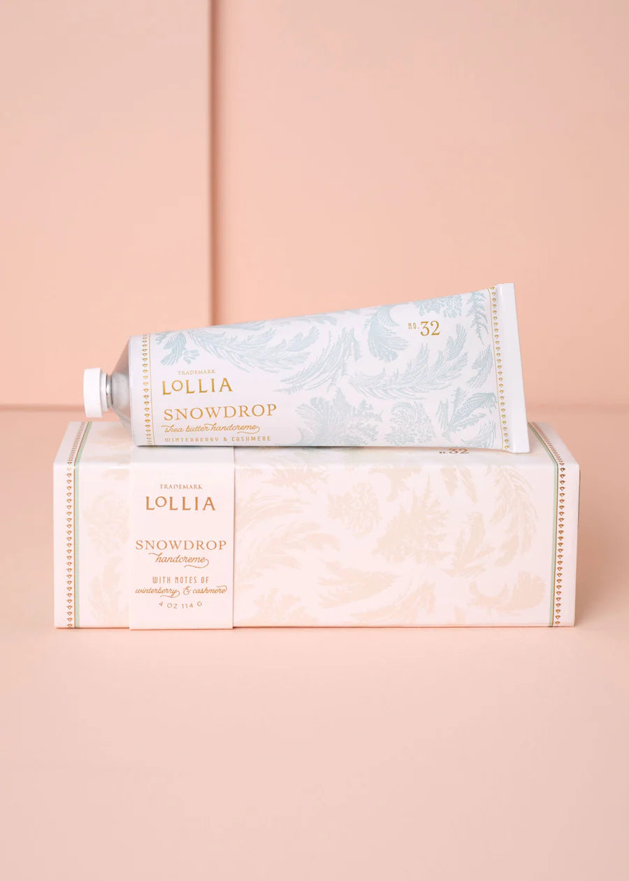 Lollia Snowdrop hand creme tube set on its box packaging on a pink background