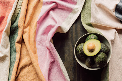 Formation Dishtowels draped on a wooden table around a bowl of avocados.