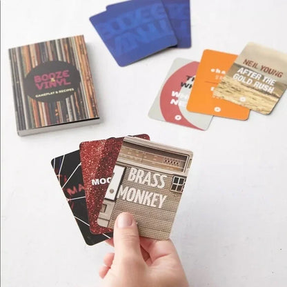 hand holding several Booze & Vinyl cards with additional cards scattered in the background