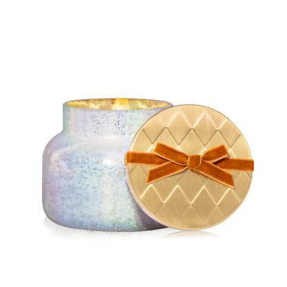 Cinnamon Cortado Artisan Winter Bazaar Signature Candle in a white shimmery glass vessel and gold lid tied with a deep orange velvet bow 