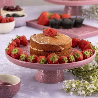 Two-layer cake on a pink cake stand with strawberries around it on a table with other baked goods