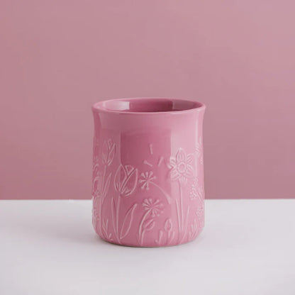 Pink ceramic utensil crock with floral patterns on a white surface and pink background