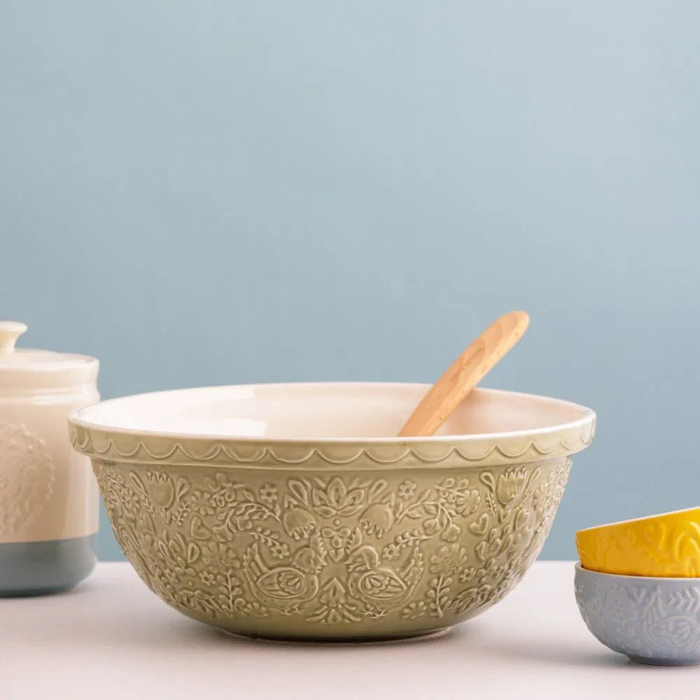 home to roost pistachio green bowl with chicken and floral embossed design set on a counter with a wooden spoon in it