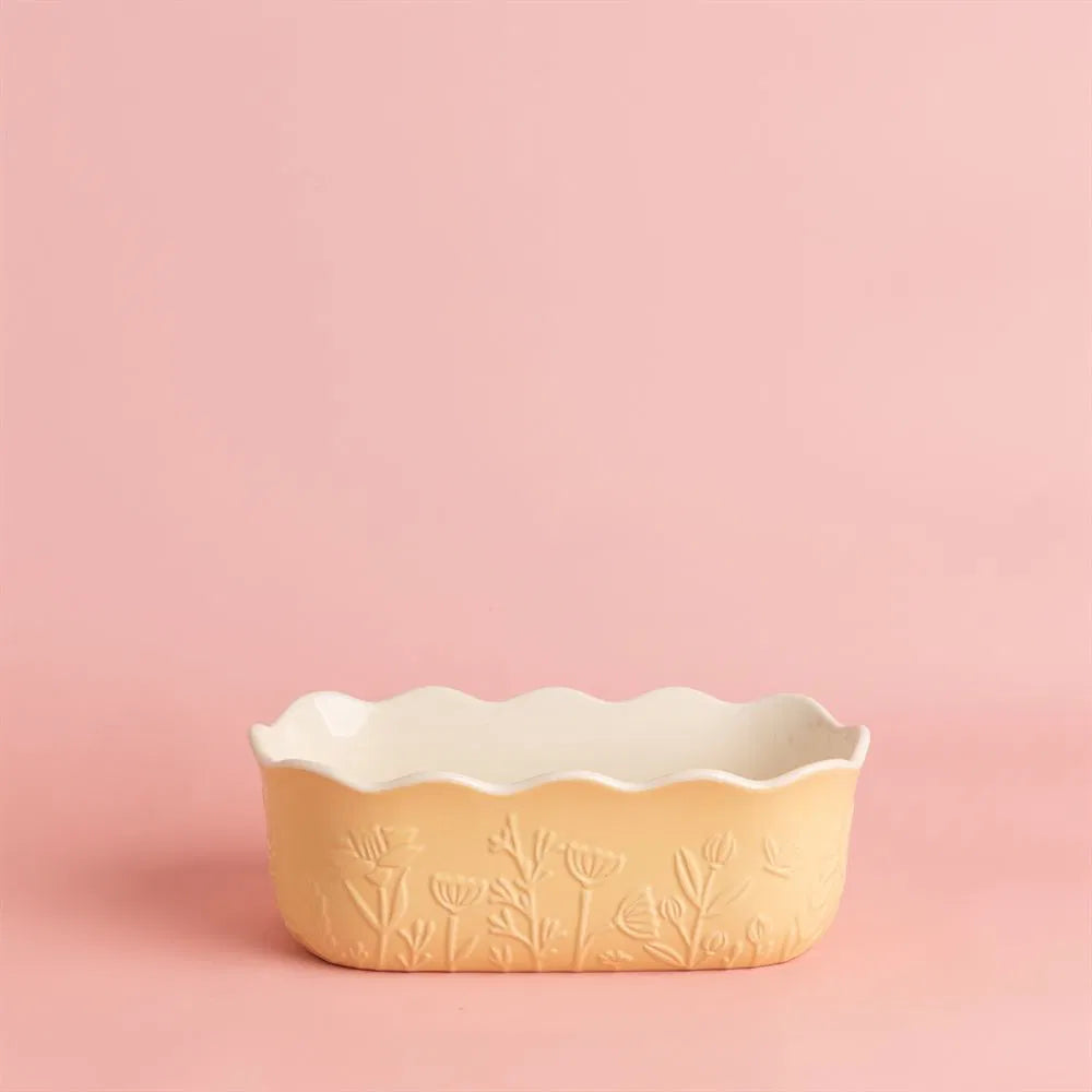 Decorative yellow loaf pan with floral embossing on a pink background