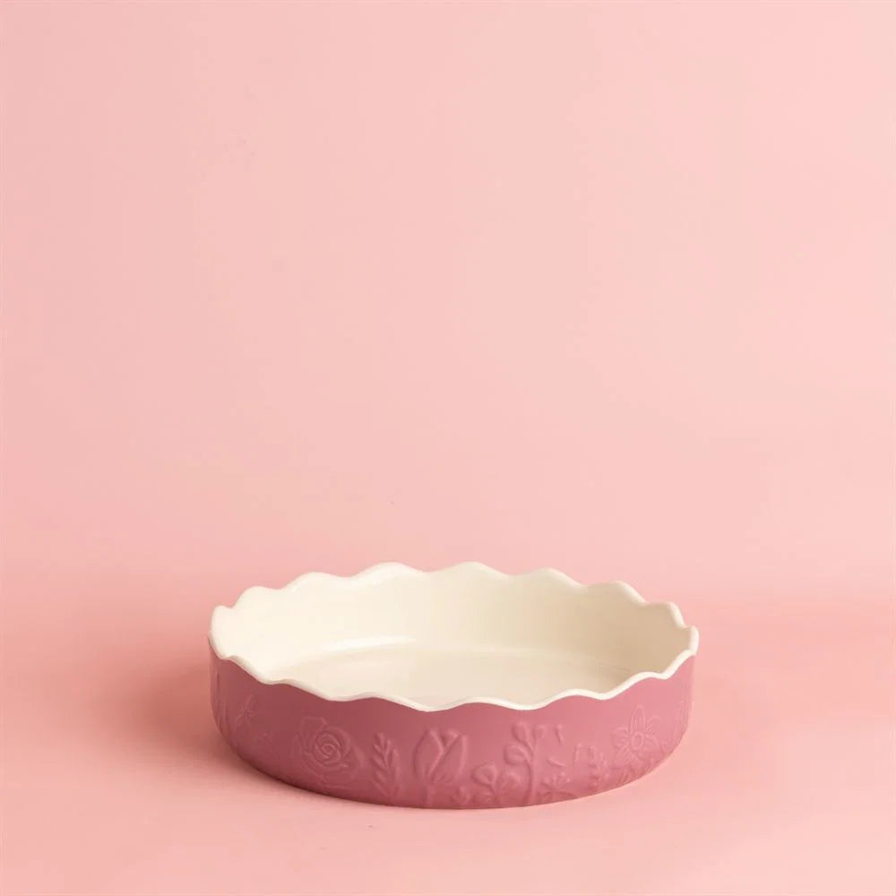 Pink ceramic pie dish with scalloped edge on a pink background