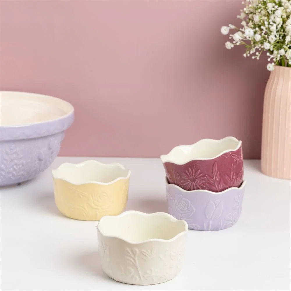 Set of small ceramic ramekins with floral patterns on a light surface against a pink background