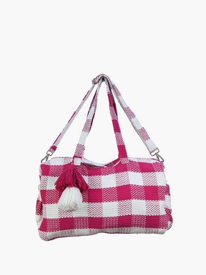 pink and white checkered weekend bag with chunky tassel hanging on handle.