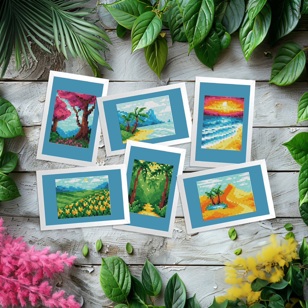 6 completed mini dazzles artworks of landscapes with blue and white mattes arranged on a wooden surface with greenery