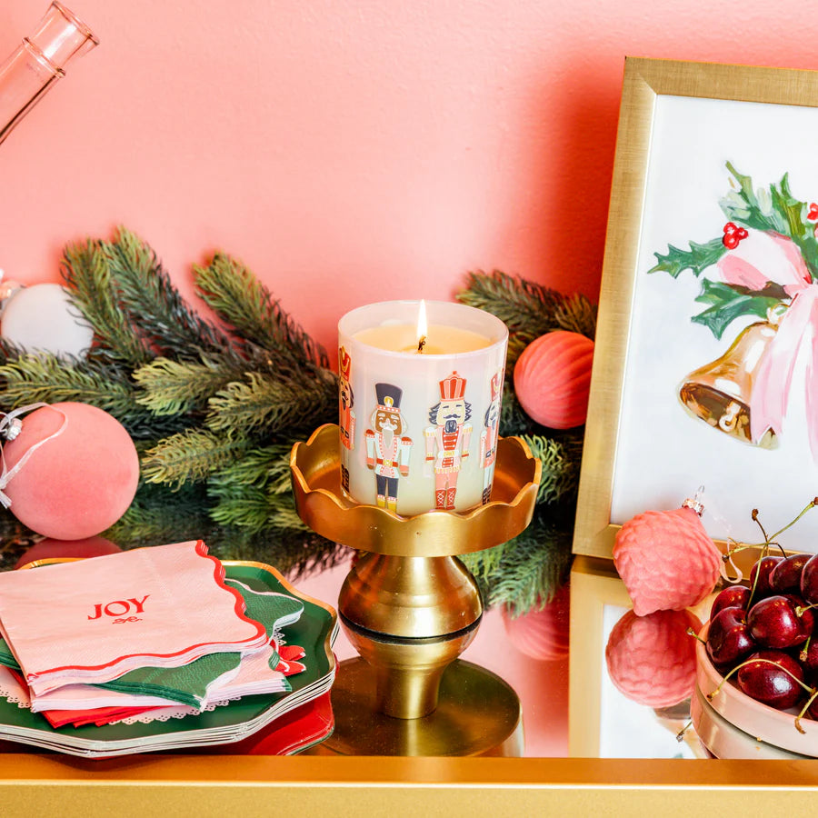 Decorative setup with a lit candle and Christmas-themed decor, on a pink background.
