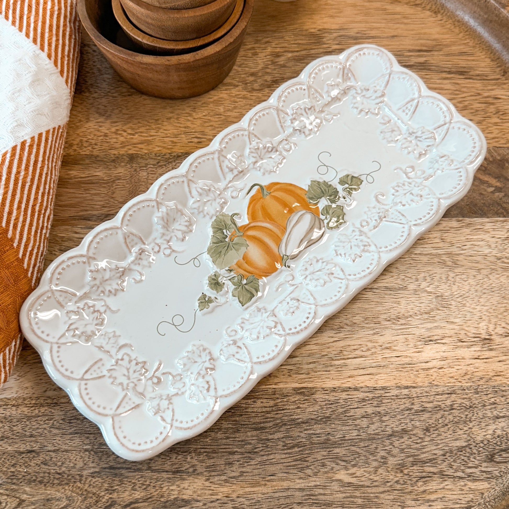A decorative tray with pumpkin designs on a wooden tray with a towel and tiny bowls.