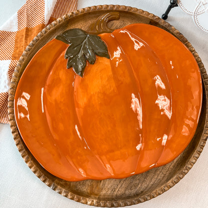 Orange pumpkin shaped platter with green leaf and brown stem on a wooden platter.