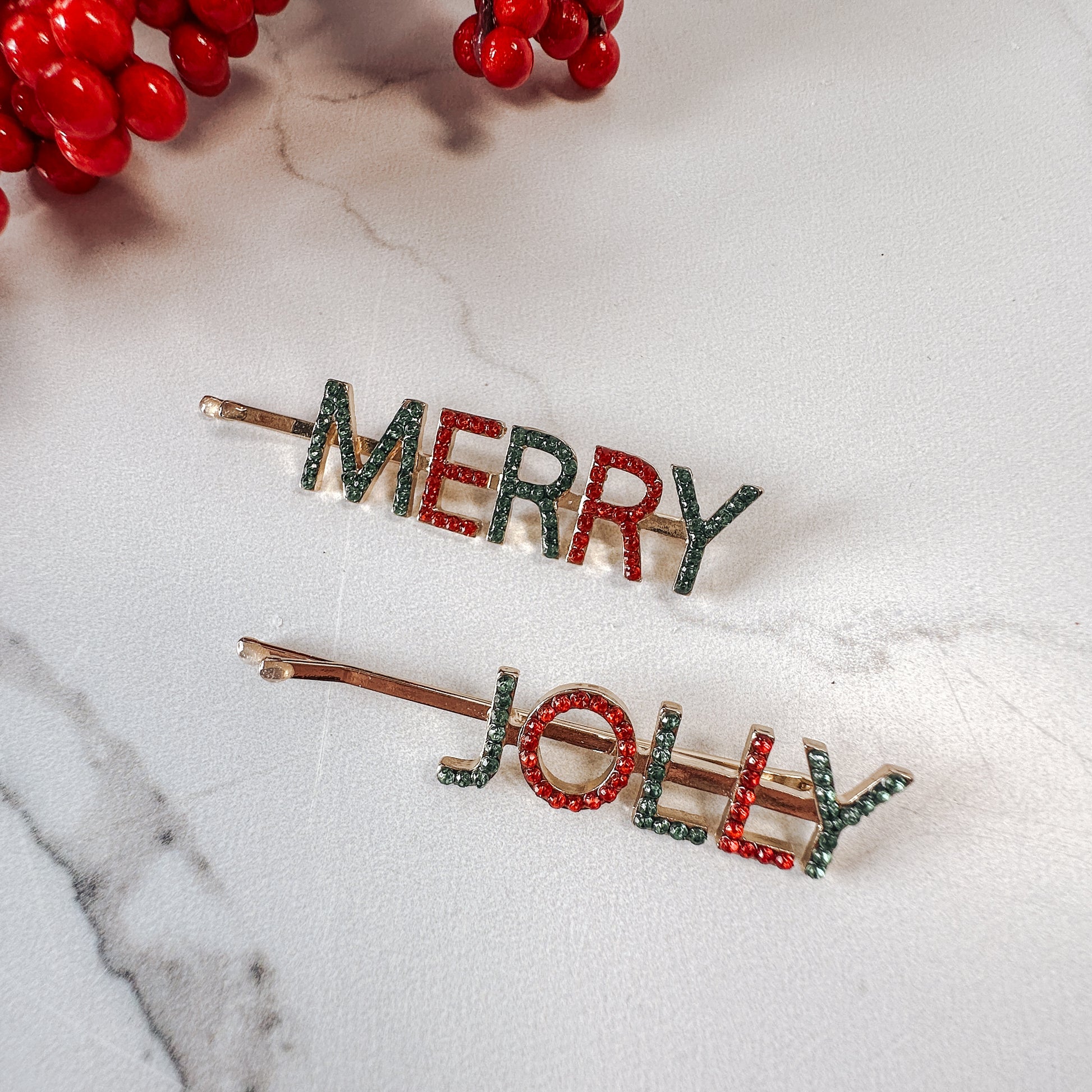 Set of two word hair clips, one says "merry" and the other says "jolly" in green and red jewel letters with gold hairpins.