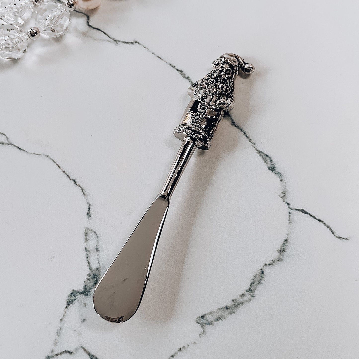 A metal spreader with santa shaped handle on a marble background.