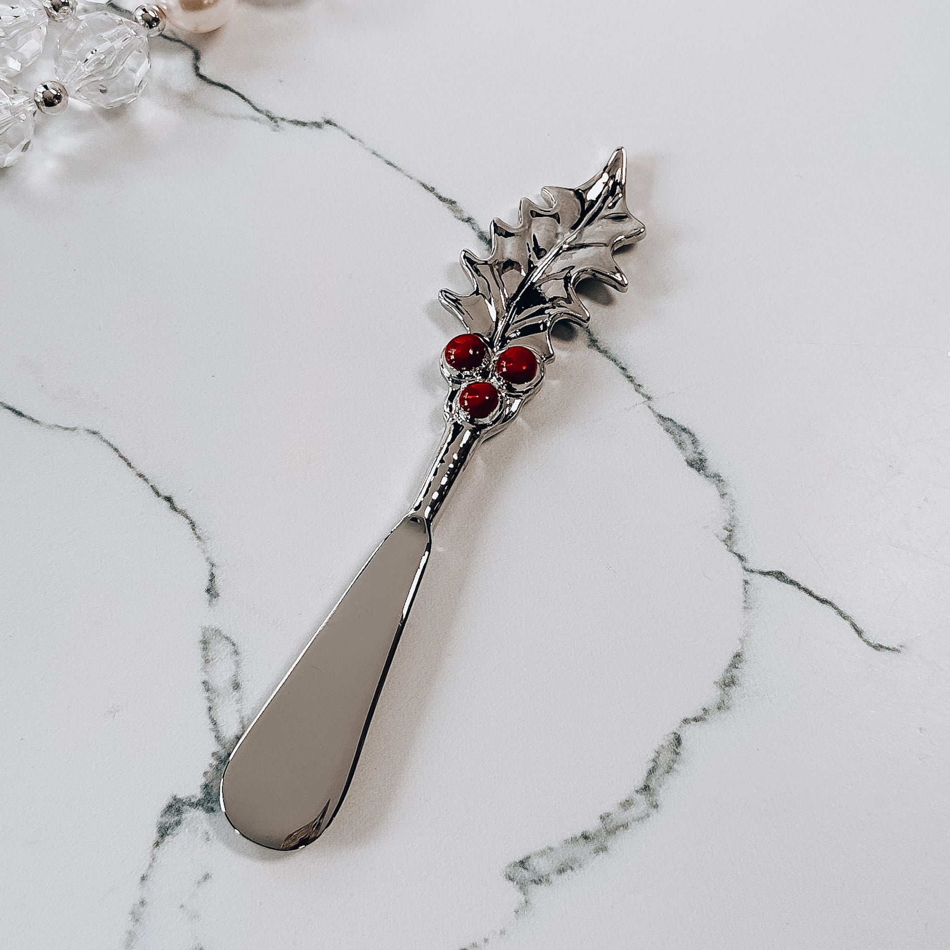 a metal spreader with holly leaf handle decorated with red berries.