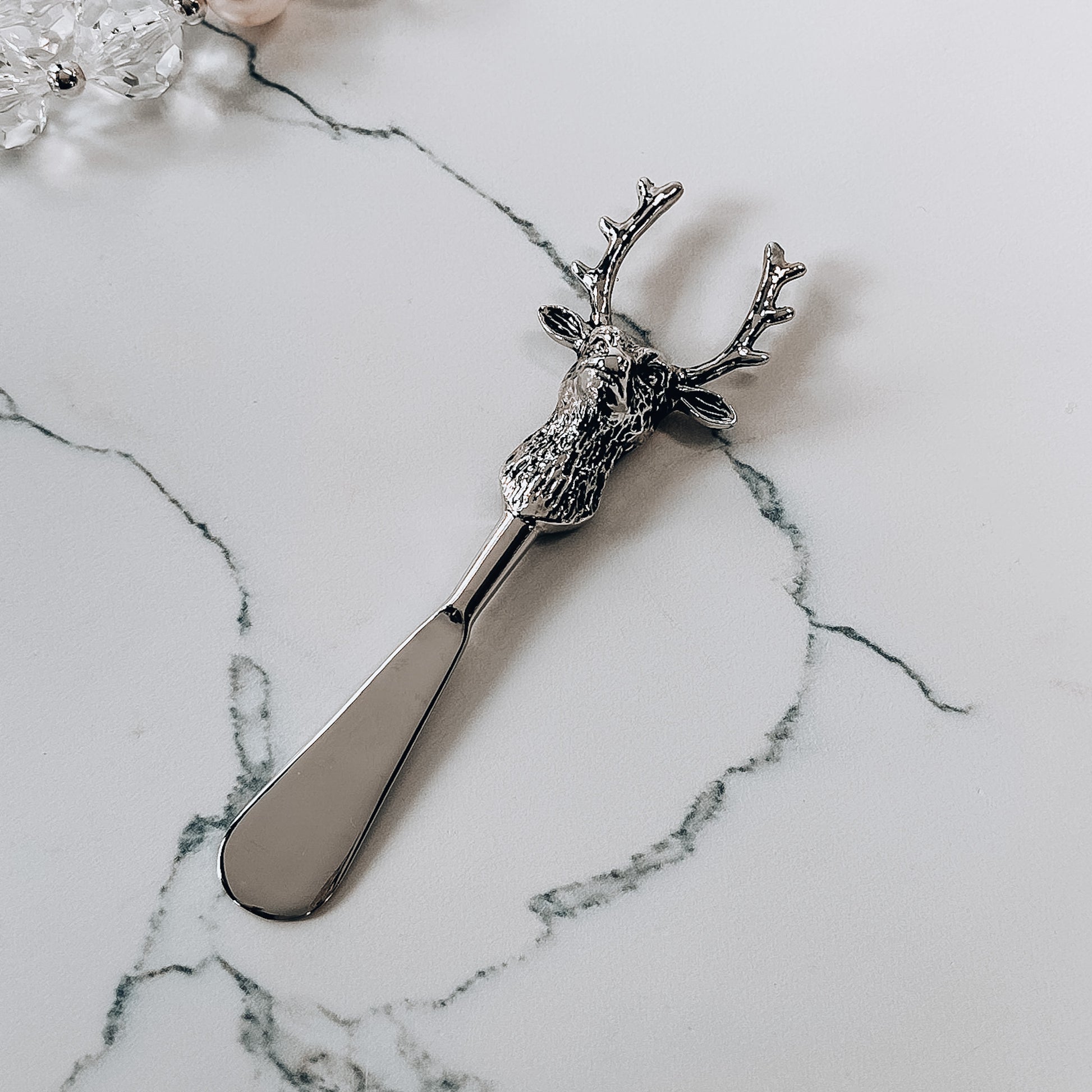 A metal spreader with deer shaped handle on a marble background.