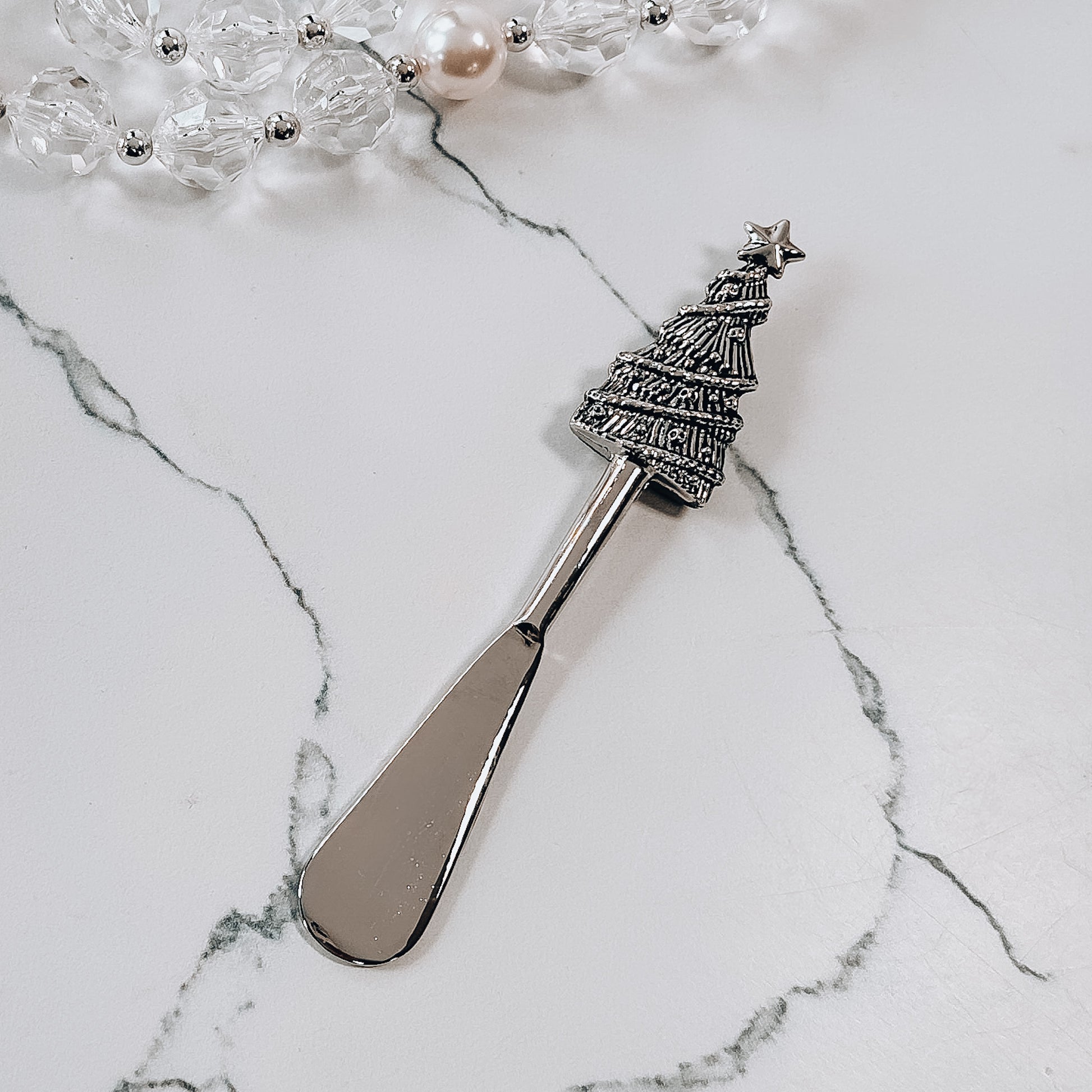 A metal tree spreader with christmas tree shaped handle on a marble background.