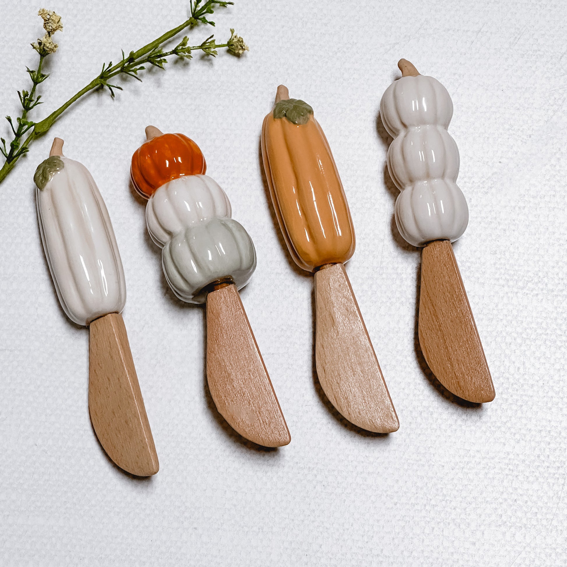 four Mud Pie Pumpkin Spreaders on a linen background with faux foliage.