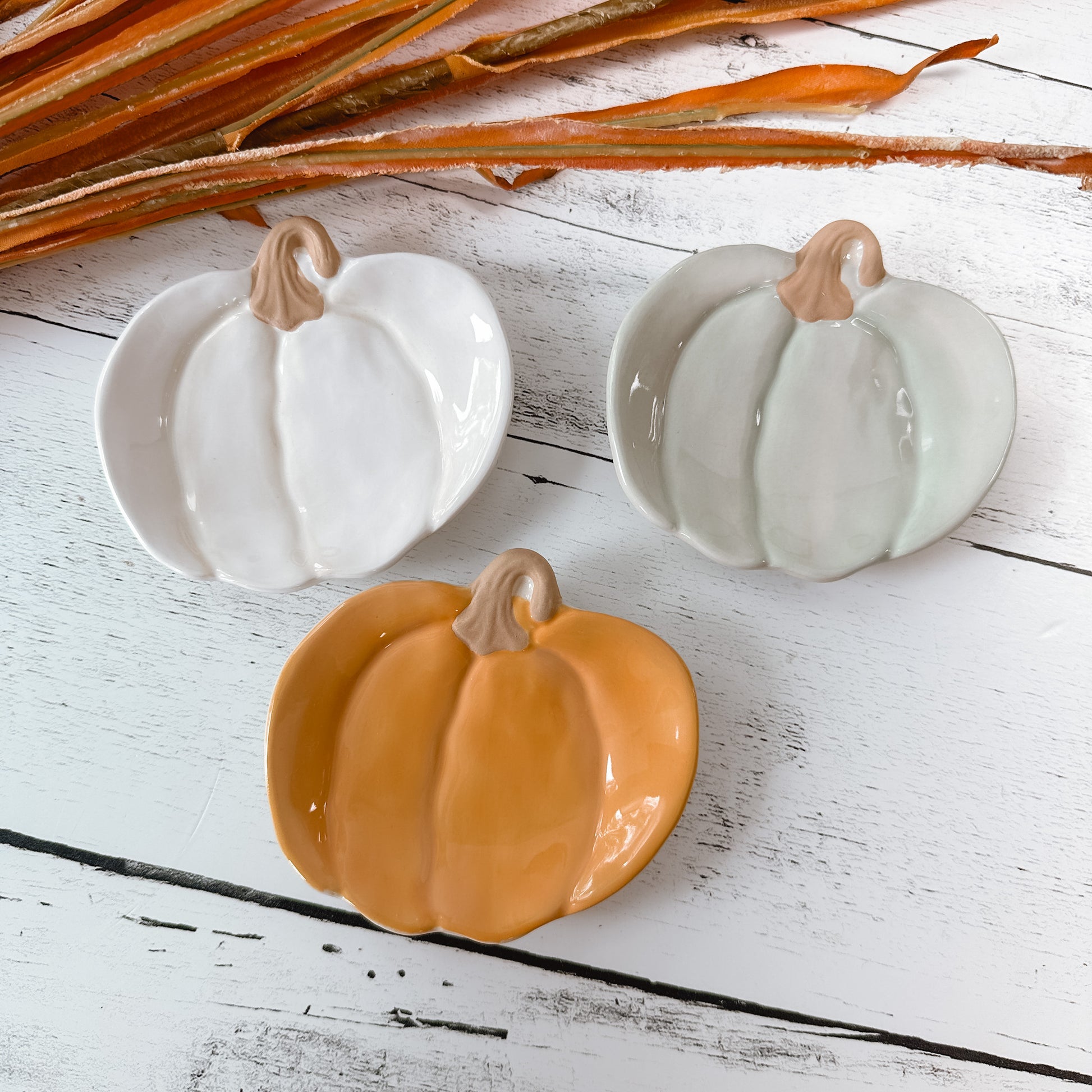 Three mud pie pumpkin shaped tidbit plates in cream, green, and orange on a wooden talbe background.