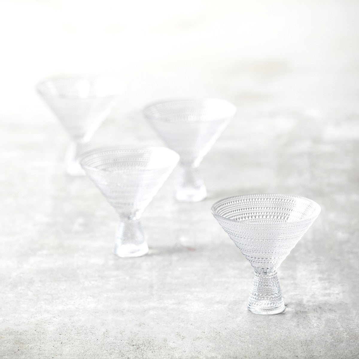 4 clear jupiter martini glasses arranged on a countertop.