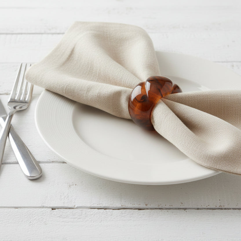 Beige napkin on a white plate with a resin tortoise napkin ring on a light wooden surface