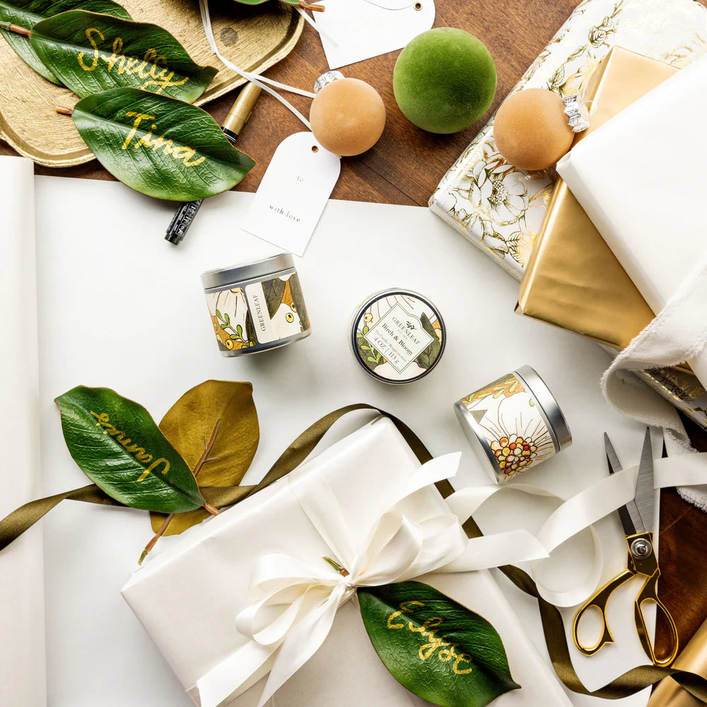 top view of a table arranged with Birch & Bloom Tin Candles, magnolia leaves, and wrapping supplies