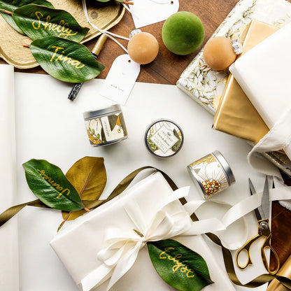 top view of a table arranged with Birch & Bloom Tin Candles, magnolia leaves, and wrapping supplies
