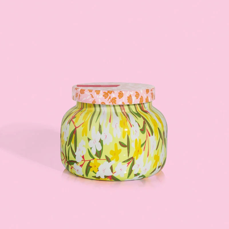 aloha orchid candle in a yellow and white floral tin with a pink floral lid on a light pink background.