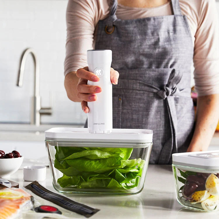 person holding vacuum pump and sealing a storage container filled with greens.