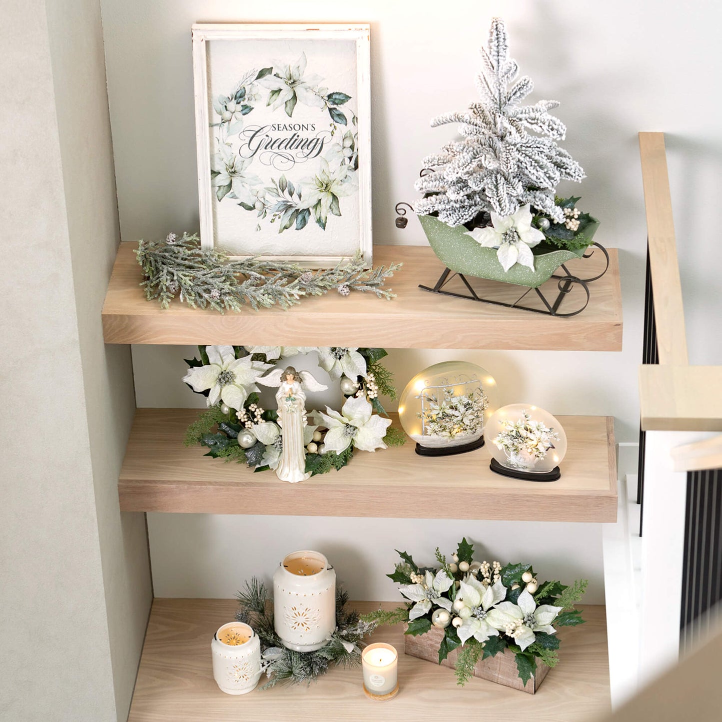 a poinsettia wall decor displayed on a shelf next to a green sleigh, frosted tree, pine sprig, wreath and more